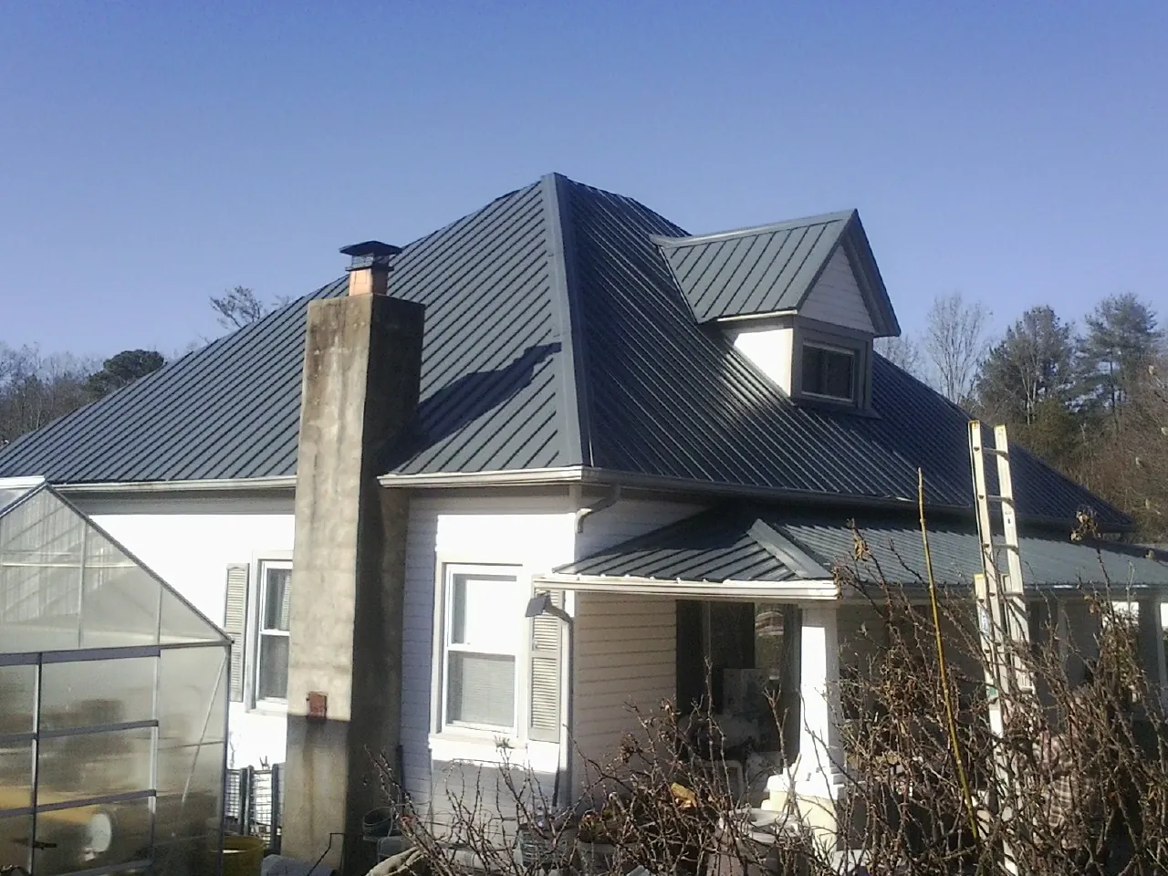 Dark blue standing seam metal roof on a white farmhouse with dormer — Slate & Tile Roof Repair by Roofing Brothers in Shorewood
