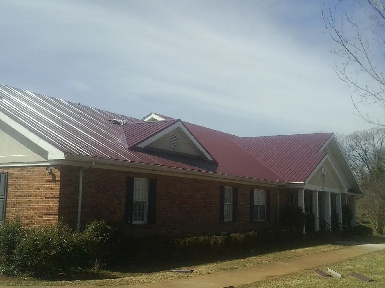 Red metal roof with gabled entries on a long brick building, from a Hail Damage Roof Repair job in Shorewood