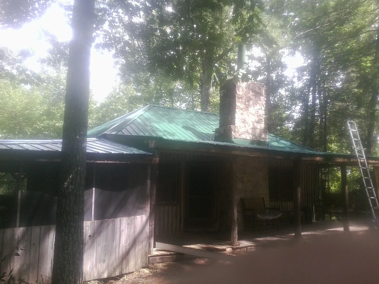 Green metal roof and stone chimney above a log cabin porch in Shorewood