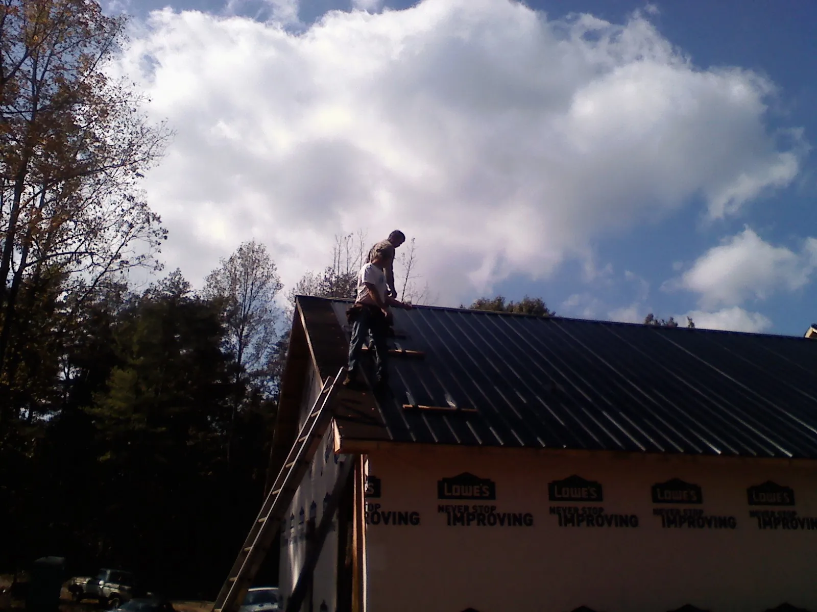 Roofer fastening dark metal panels high against a cloudy sky, from a Roof Inspection job in Shorewood