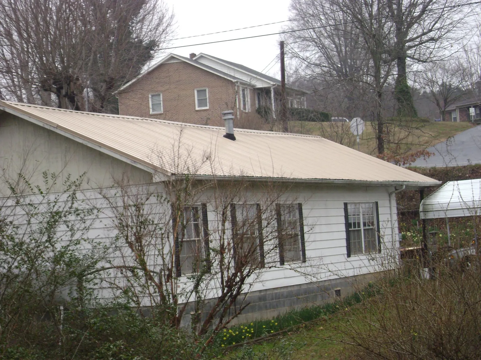 Tan metal roof on a white sided house set into a hillside — Commercial Roofing by Roofing Brothers in Shorewood